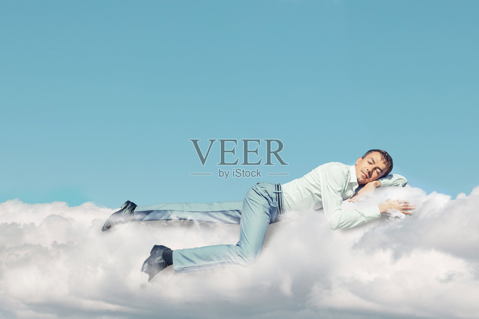 一个穿着白衬衫和蓝裤子的年轻人，在蓝天下蓬松的白云上甜蜜地睡觉。照片摄影图片