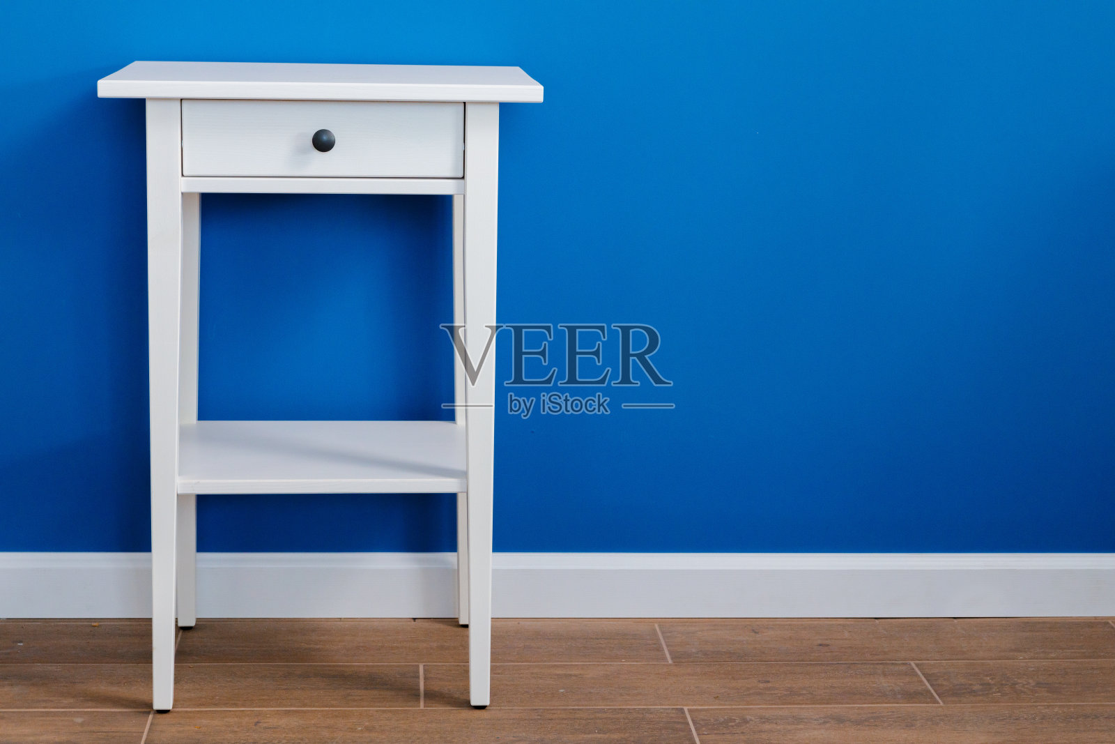 白色的木质床头柜靠着蓝色的墙照片摄影图片