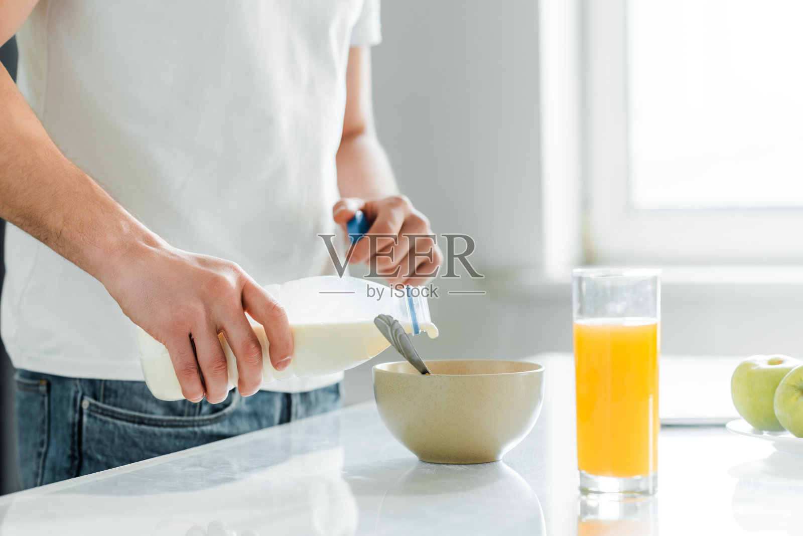 一个人把牛奶倒在碗里，旁边是桌上的橙汁和苹果照片摄影图片