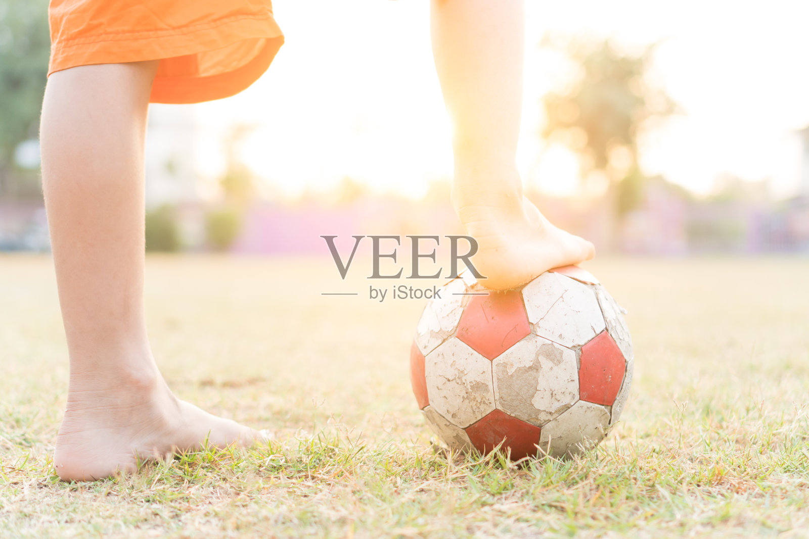 一个小男孩的腿上有一个旧的红白相间的足球在早上。照片摄影图片