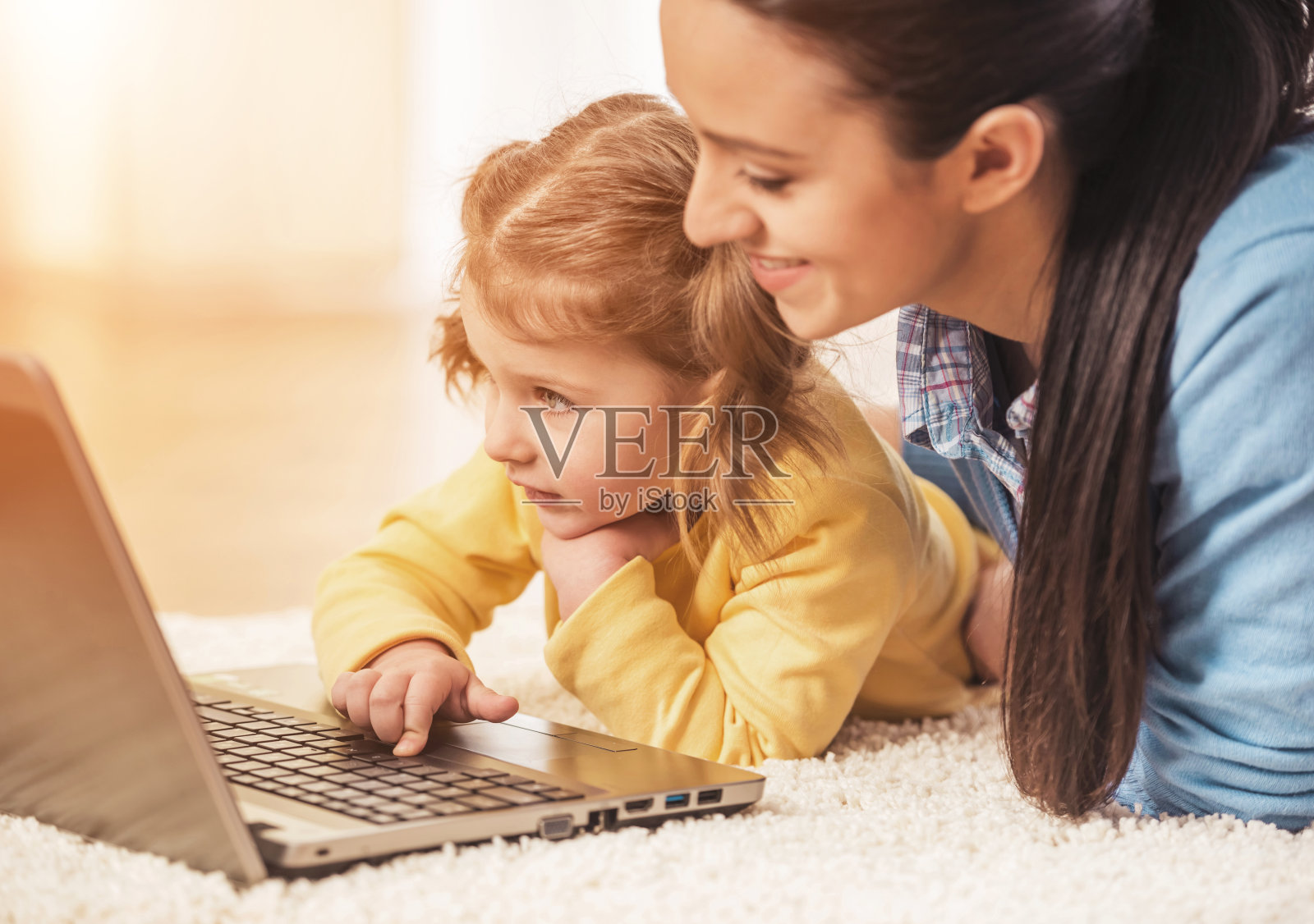 快乐的母亲和女儿在地毯上和笔记本电脑。照片摄影图片