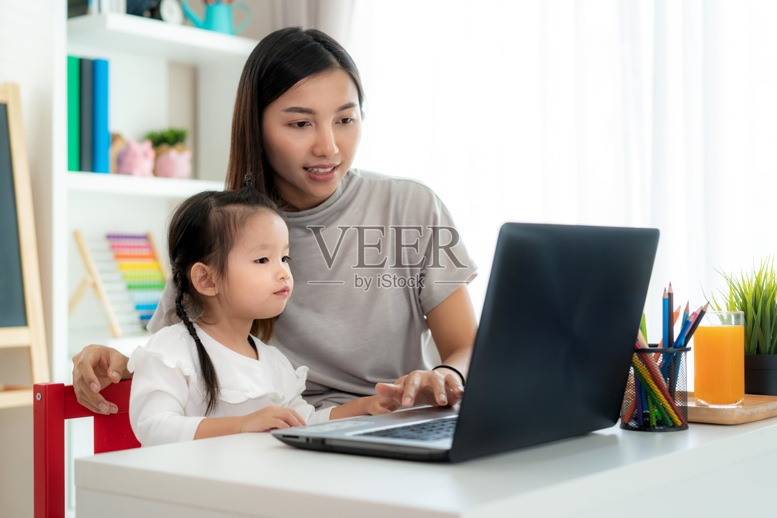 亚洲幼稚园女孩与母亲视频会议电子学习与教师在客厅笔记本电脑在家里。在家教育和远程学习，在线，教育和互联网。照片摄影图片