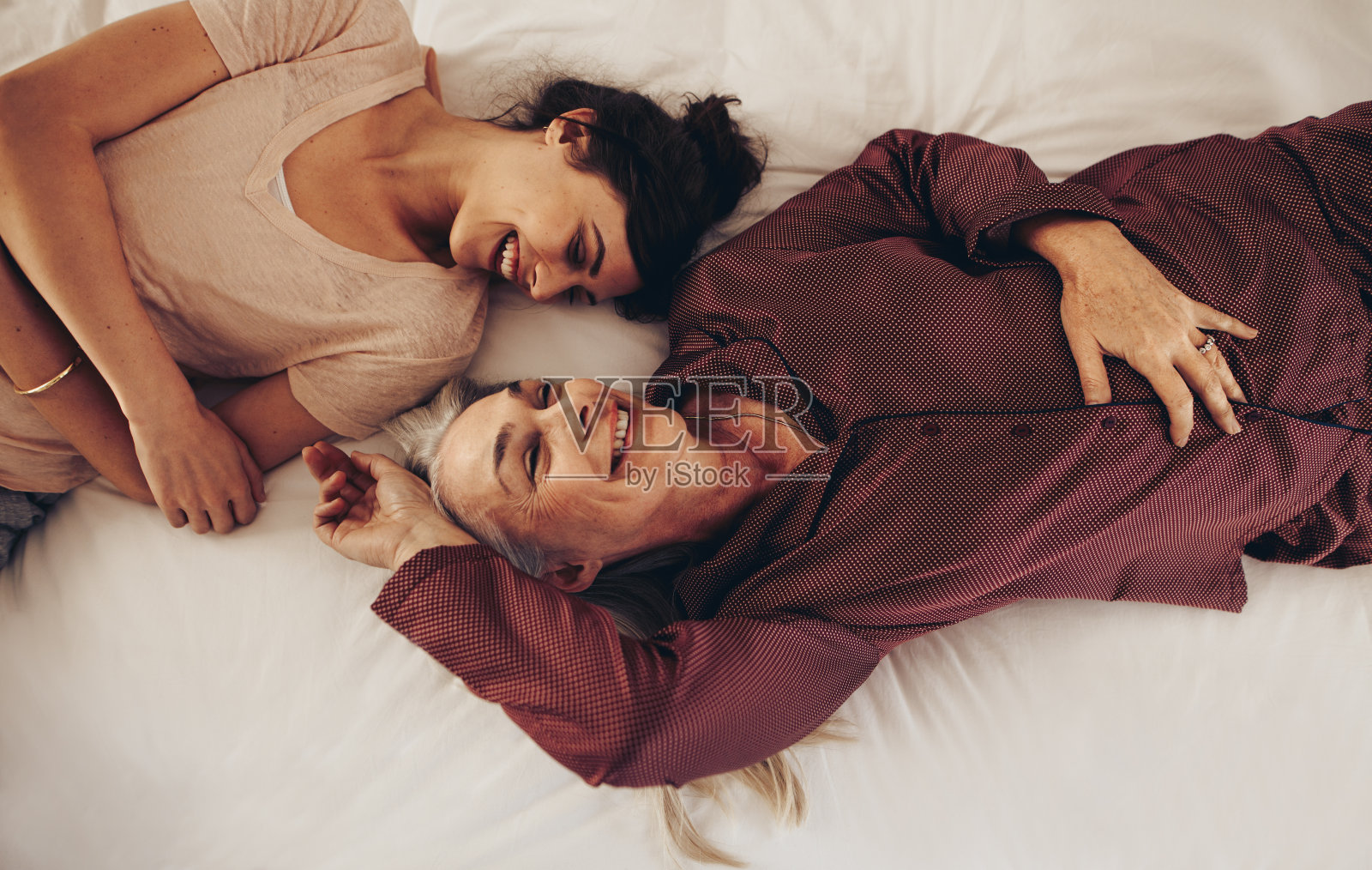 俯视图微笑的母亲和女儿躺在床上面对着对方照片摄影图片