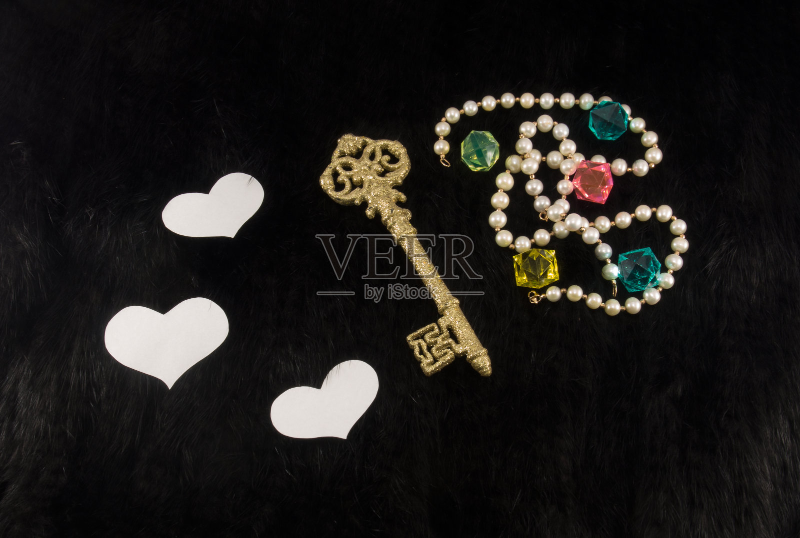 老金钥匙与白纸心和珍珠项链和彩色塑料宝石在黑色毛皮背景照片摄影图片