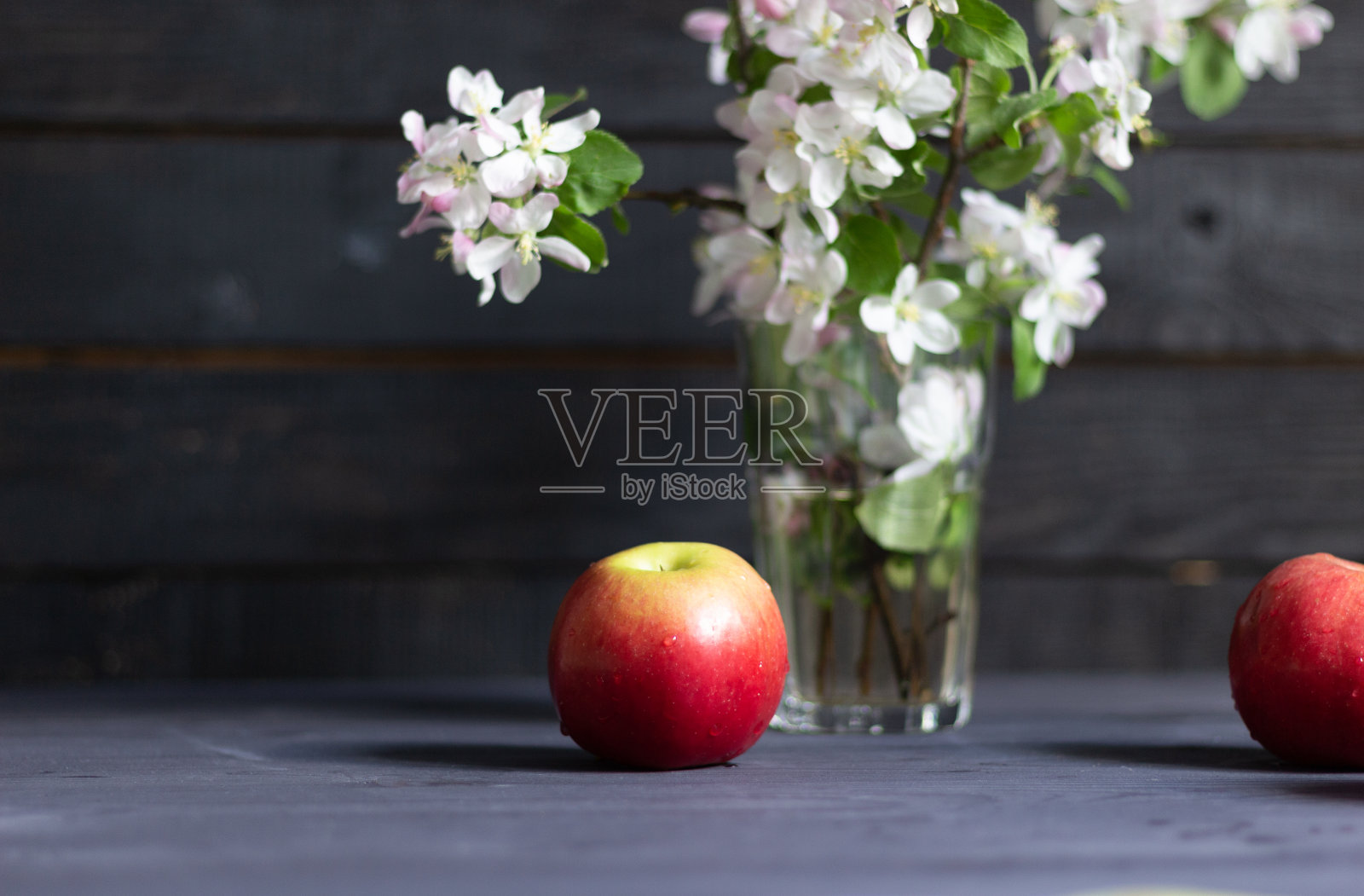 成熟的红苹果果实和苹果树枝与玫瑰和白色的花和绿色的叶子花瓶在黑色的木制背景照片摄影图片