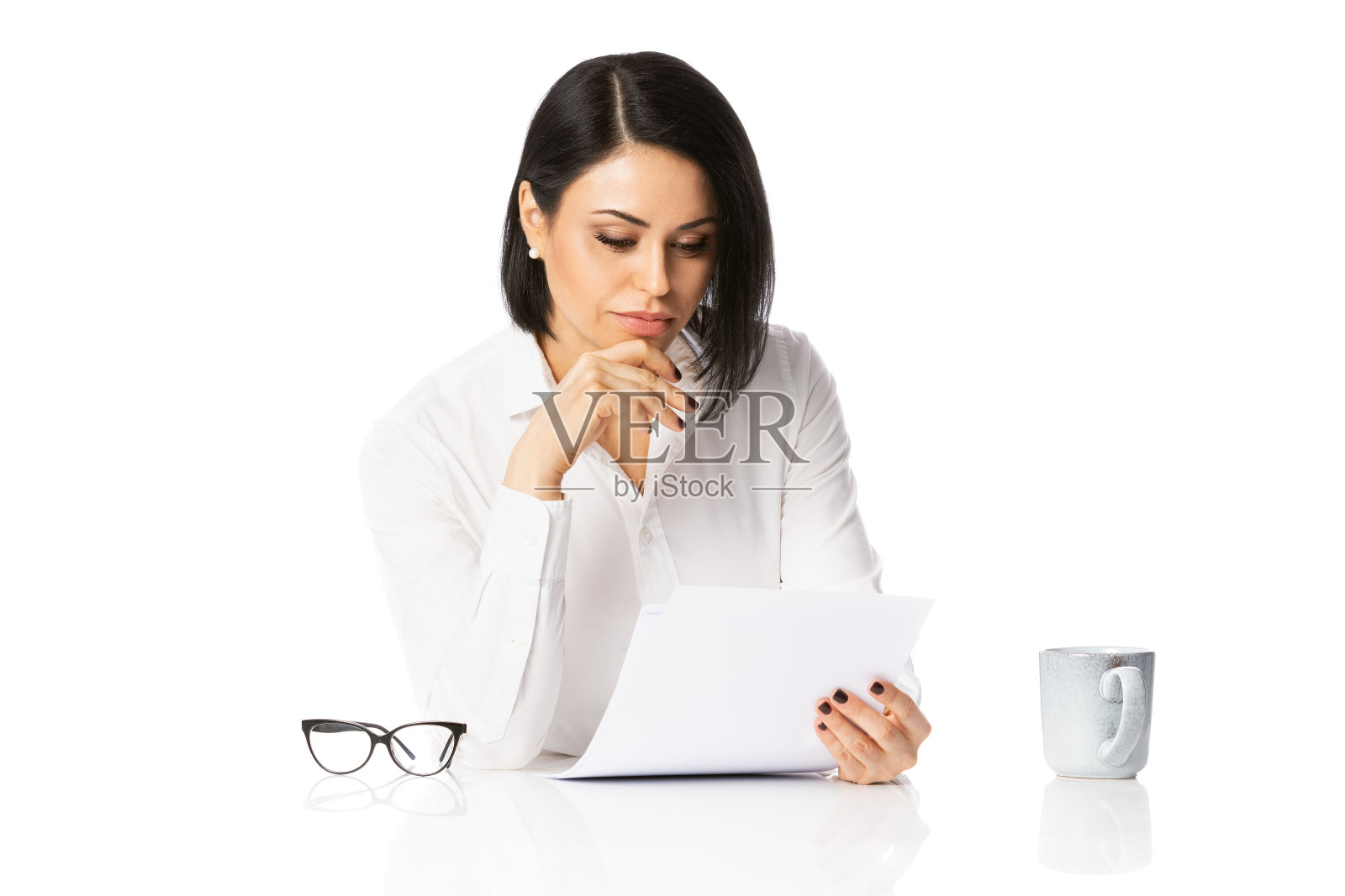 沉思的年轻商务女性穿着白衬衫在她的桌子上与文件，写笔记。成就事业理念。孤立的白色背景照片摄影图片