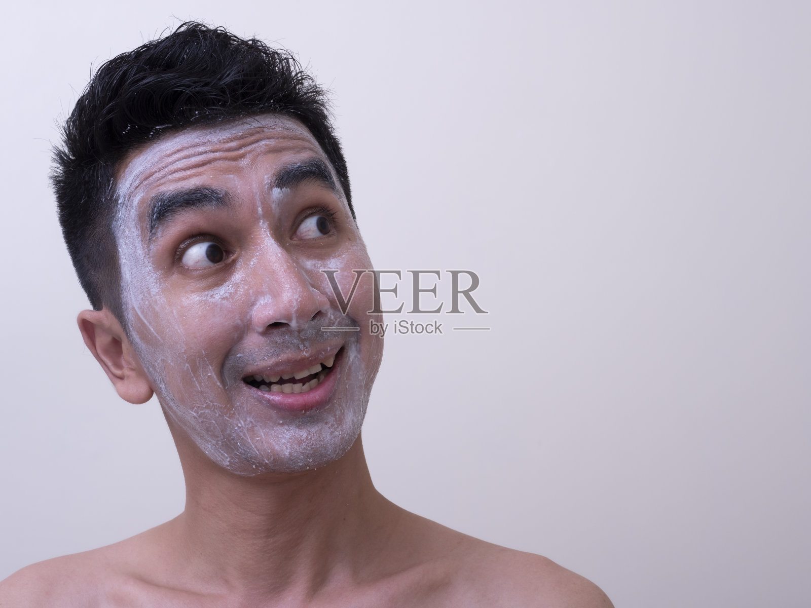 亚洲英俊的年轻男子在他的脸上涂抹霜与笑脸，皮肤护理的概念照片摄影图片