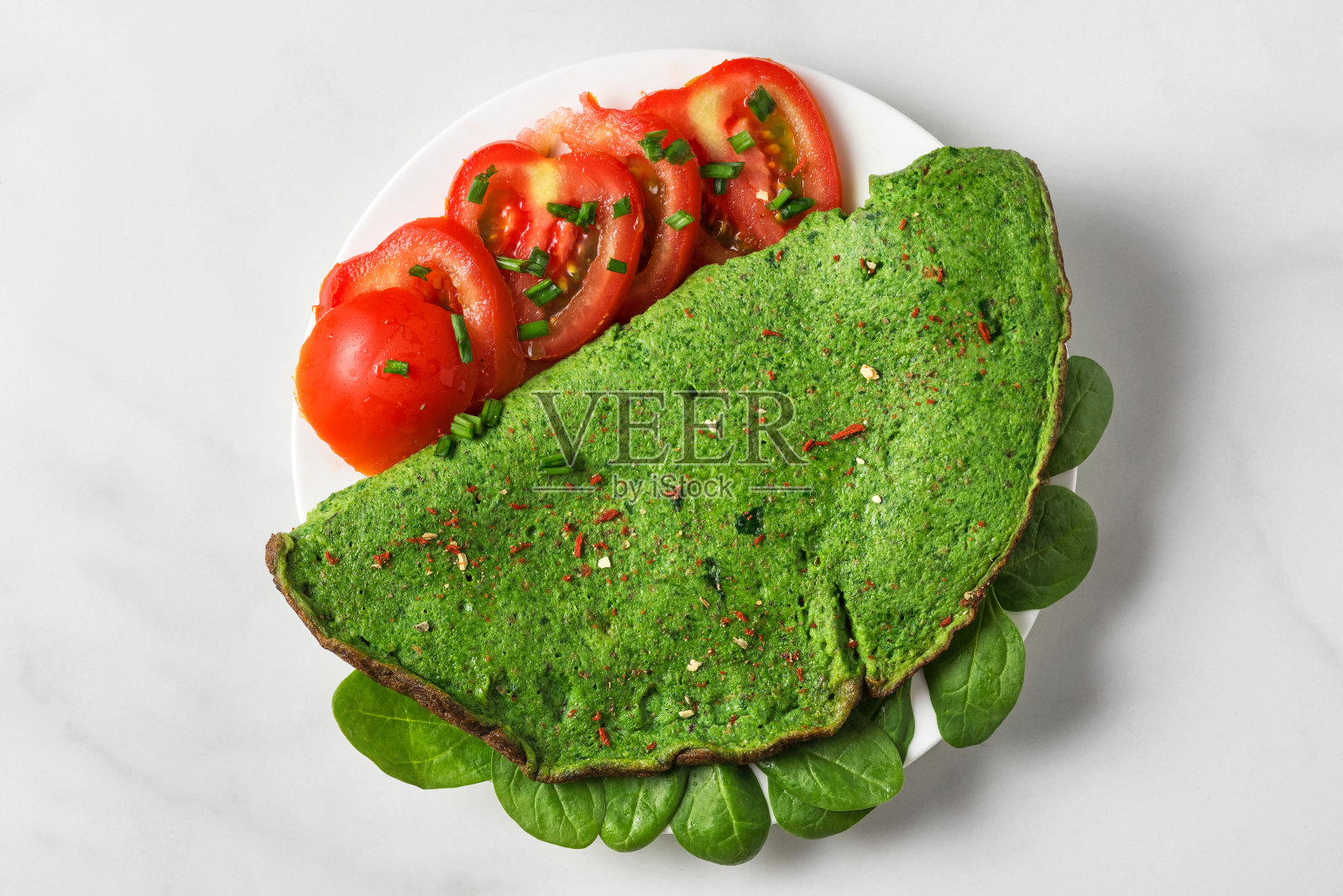 用西红柿、香料和香草制作的绿色菠菜煎蛋卷，以白色大理石为背景。酮类的减肥食品照片摄影图片