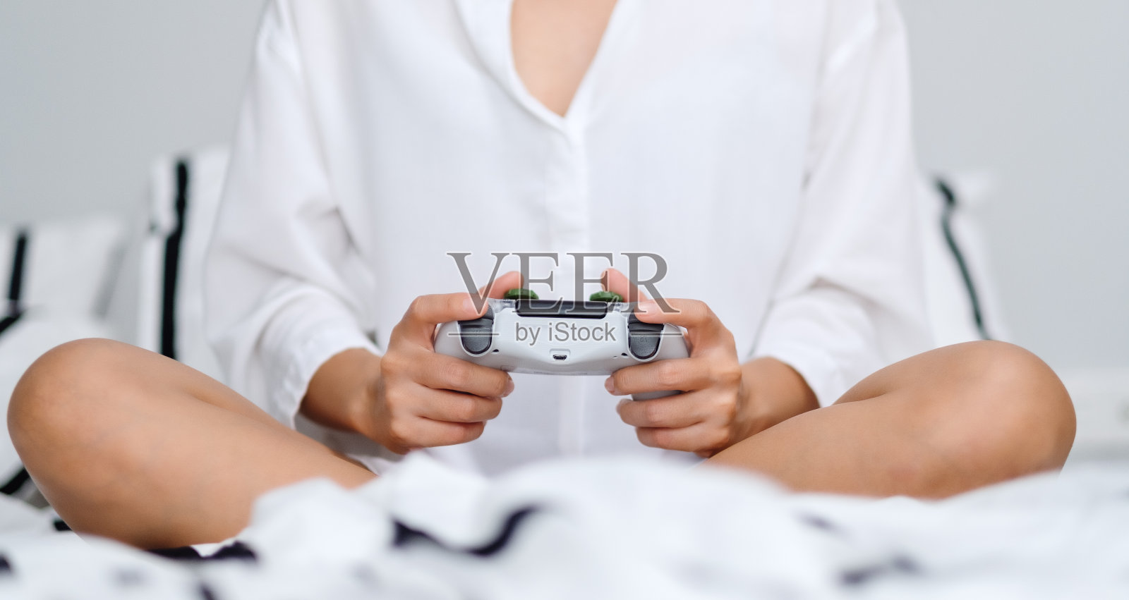 一个女人拿着游戏控制器玩游戏，坐在家里舒适的白色床上照片摄影图片