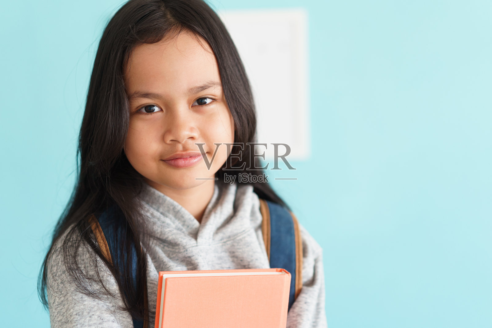 快乐的亚洲小女孩脸上的微笑，亚洲孩子拿着书和背包，一个孩子的肖像看着相机。概念背包去学校照片摄影图片