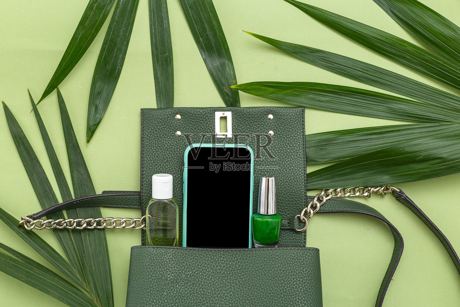 手提包，手机，指甲油和自然树叶在绿色的背景。单色。俯视图照片摄影图片