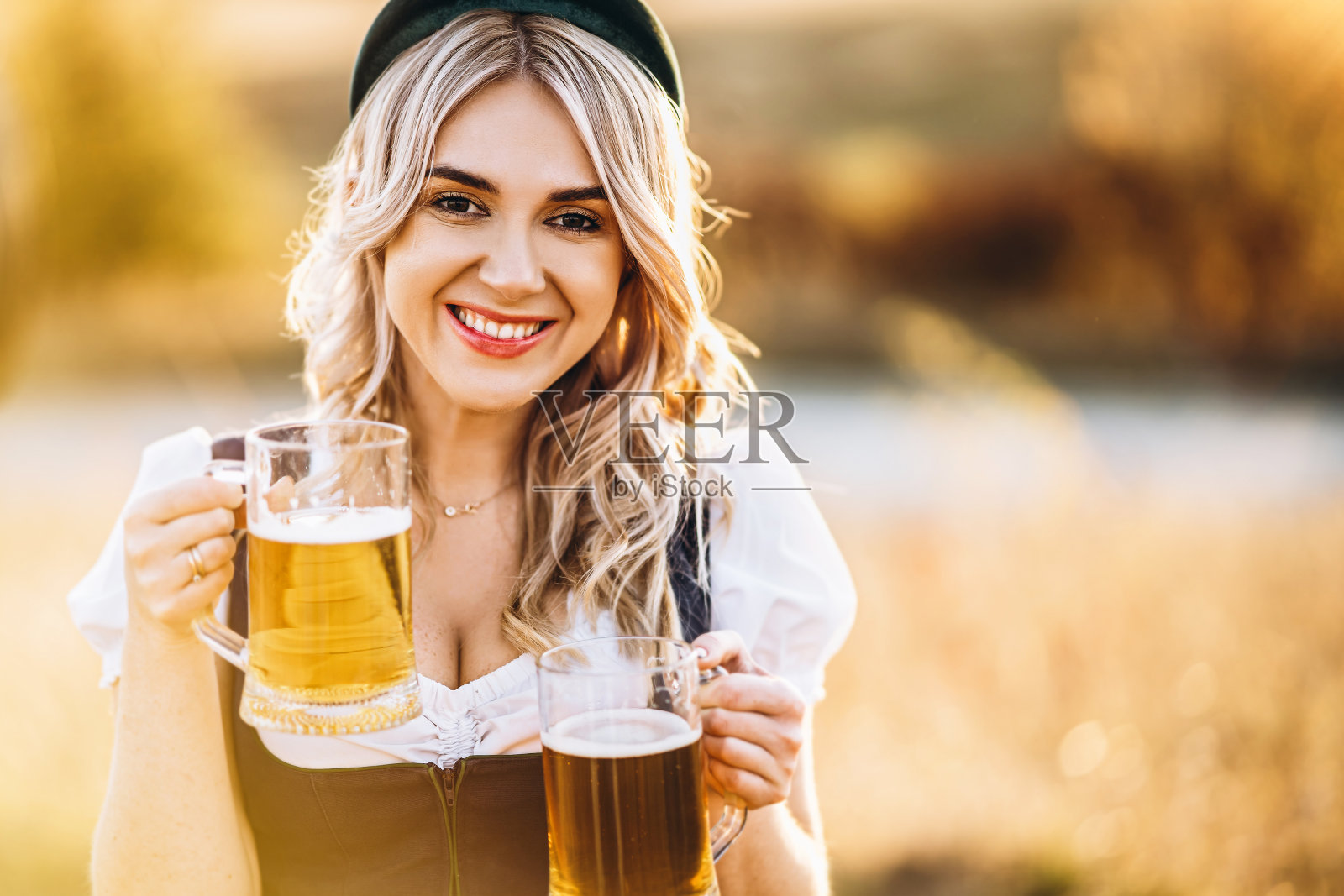 金发碧眼，穿着紧身连衣裙，传统的节日服装，在野外拿着两杯啤酒照片摄影图片