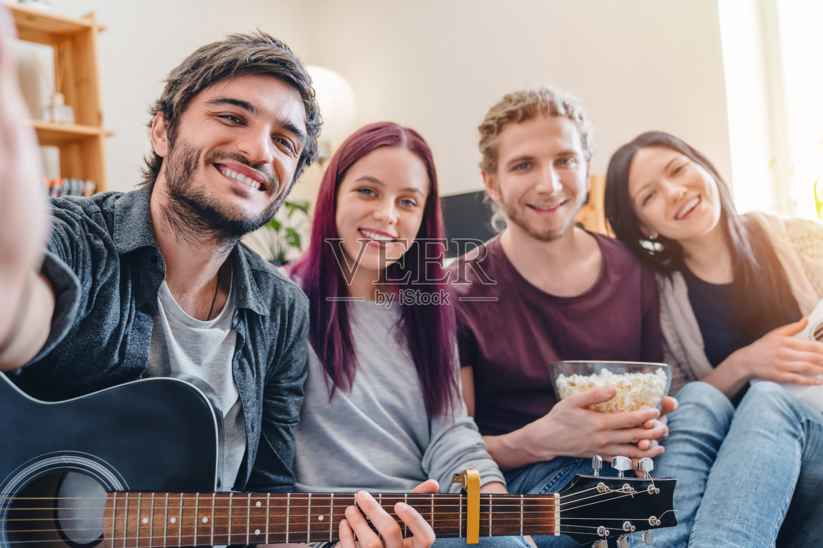 微笑的朋友们在不经意的沙发上用吉他自拍照片摄影图片