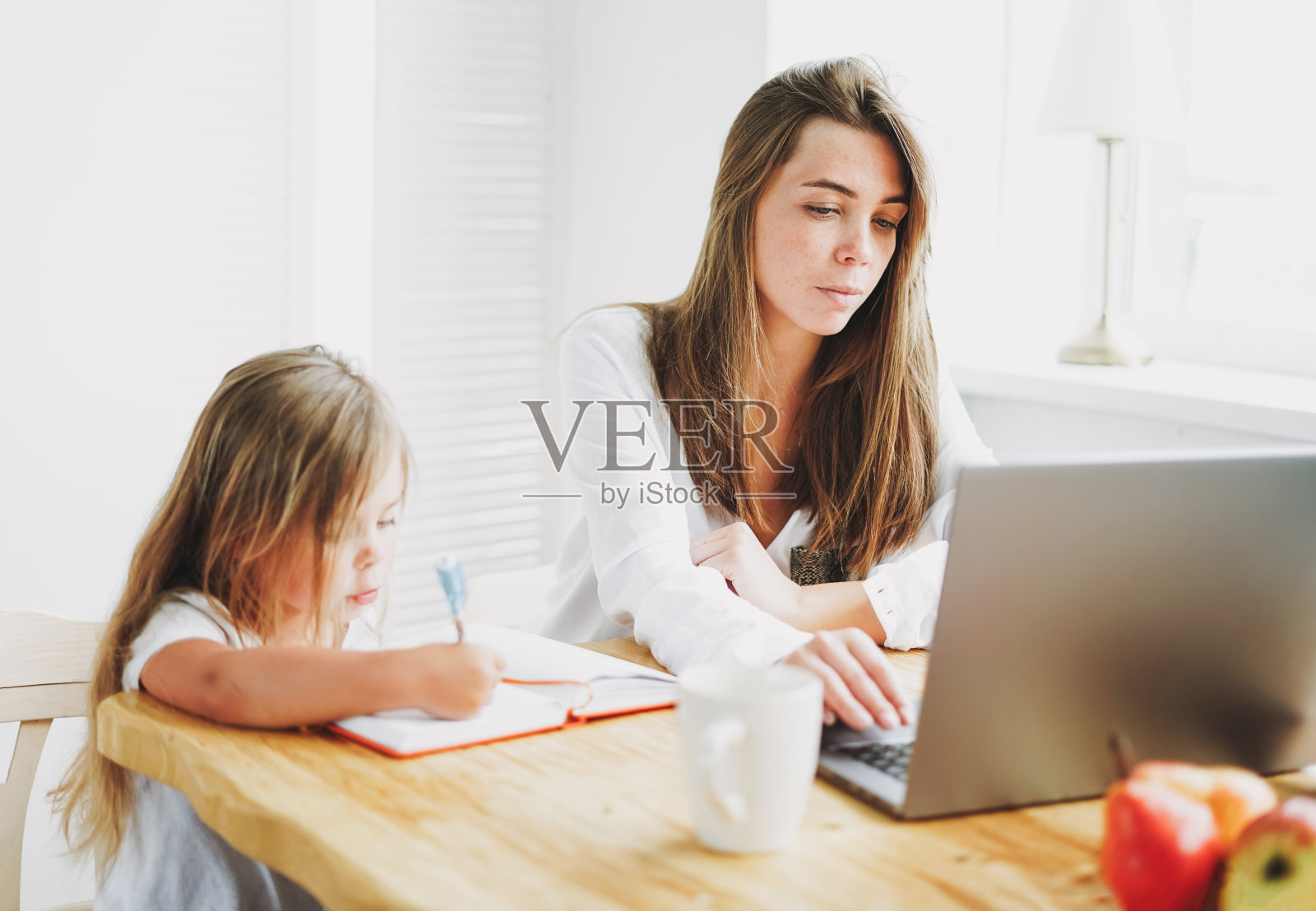 工作妈妈的自由职业者在笔记本电脑上，小女儿在家里的桌子上画画照片摄影图片