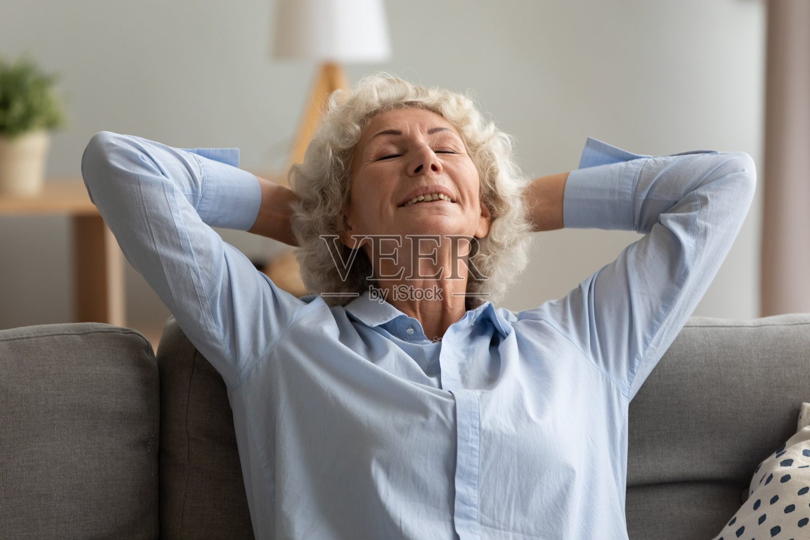 平静的老妇人把双手放在脑后，在沙发上放松照片摄影图片