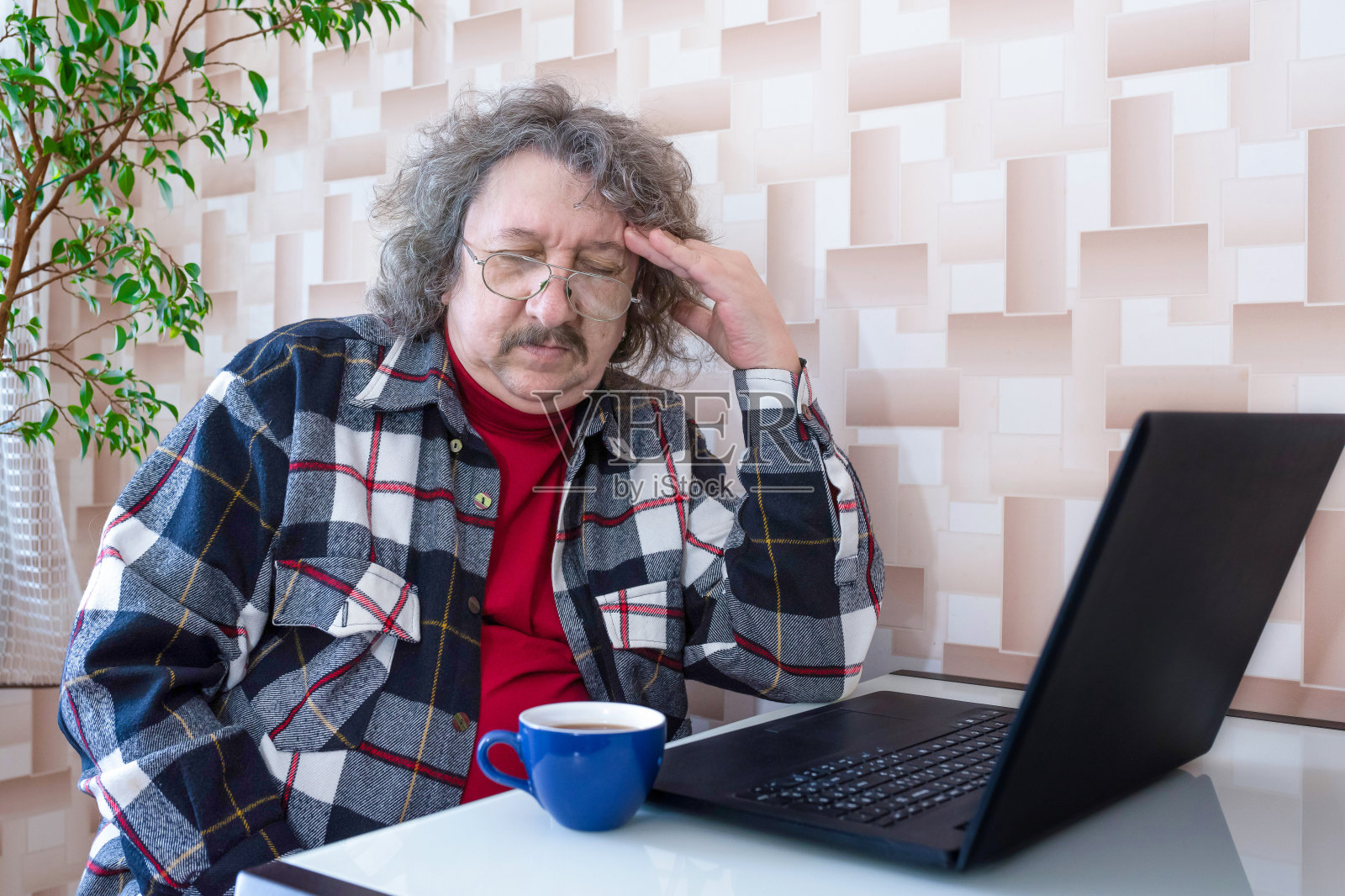 都是疲惫的老人在长时间工作后头痛的笔记本电脑上坐着。照片摄影图片