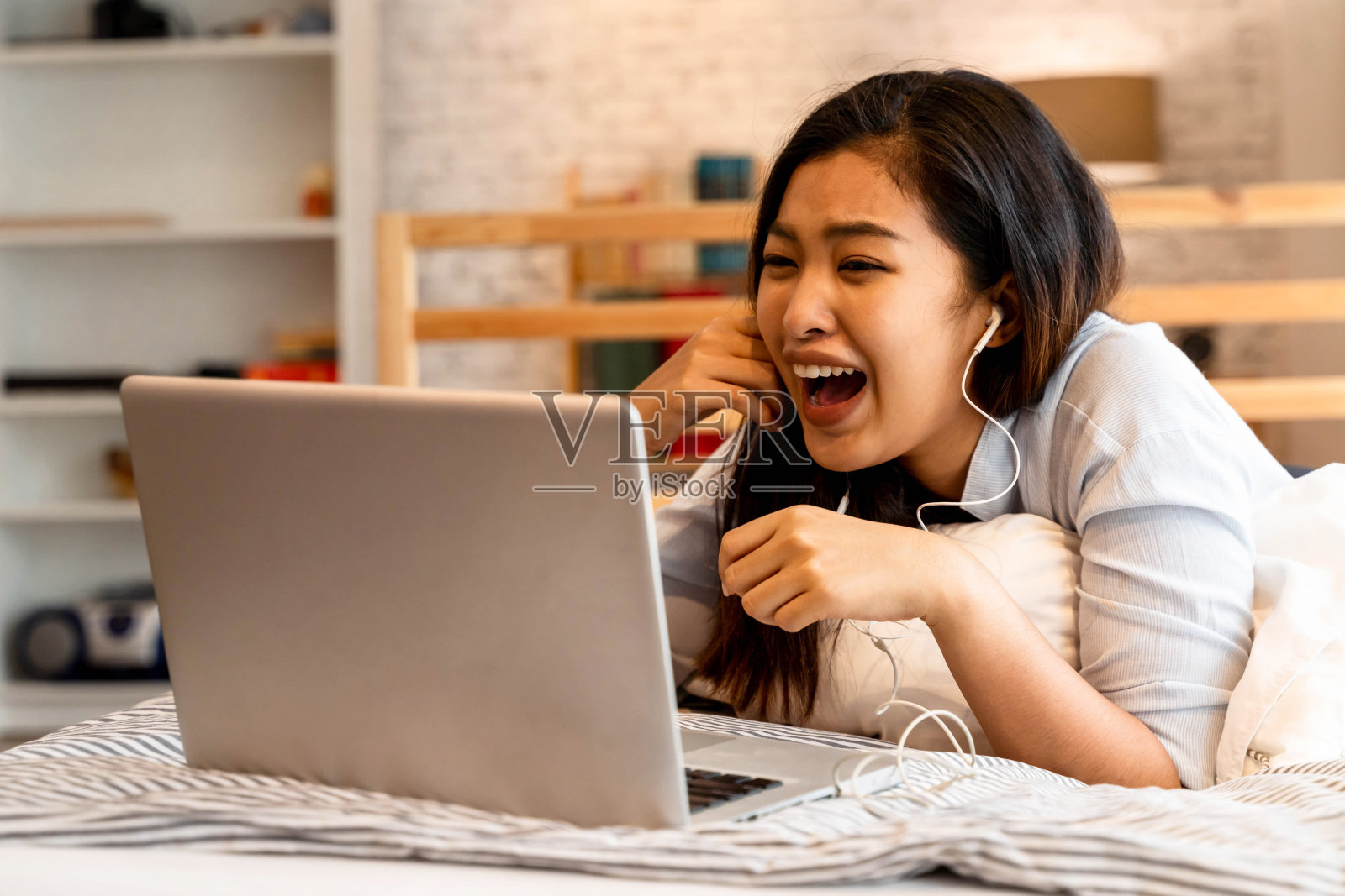 年轻微笑的亚洲妇女在休闲服装和躺在床上的笔记本电脑。女性自由职业者在家用笔记本工作。照片摄影图片