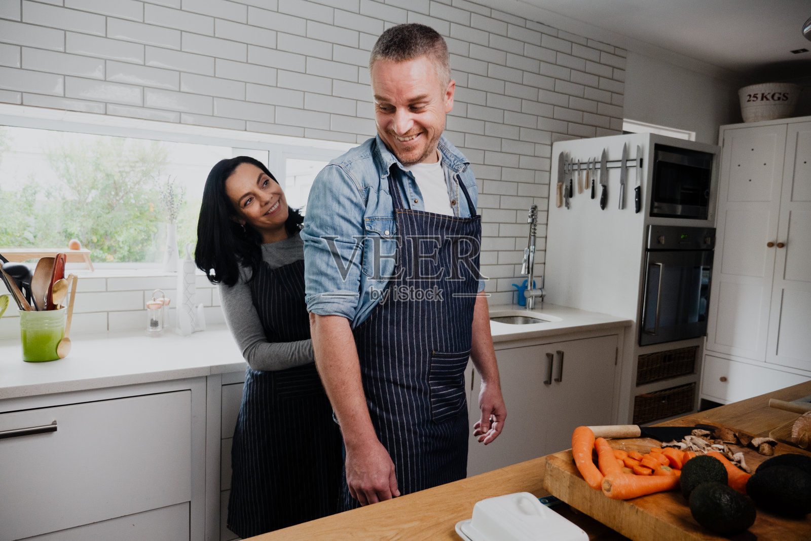 年轻夫妇一起做饭，妻子在厨房帮丈夫系围裙照片摄影图片