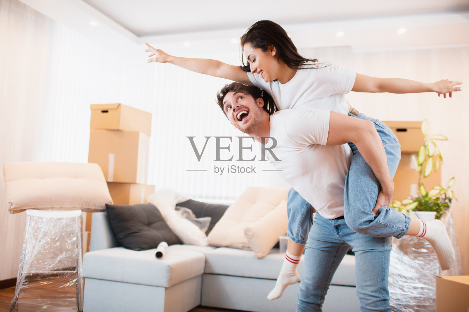 H高兴夫妻俩一起打旋摇摆搬家到自己的公寓，搬家概念。喜出于色的年轻夫妇在搬家的日子里，在纸板盒附近跳舞。照片摄影图片