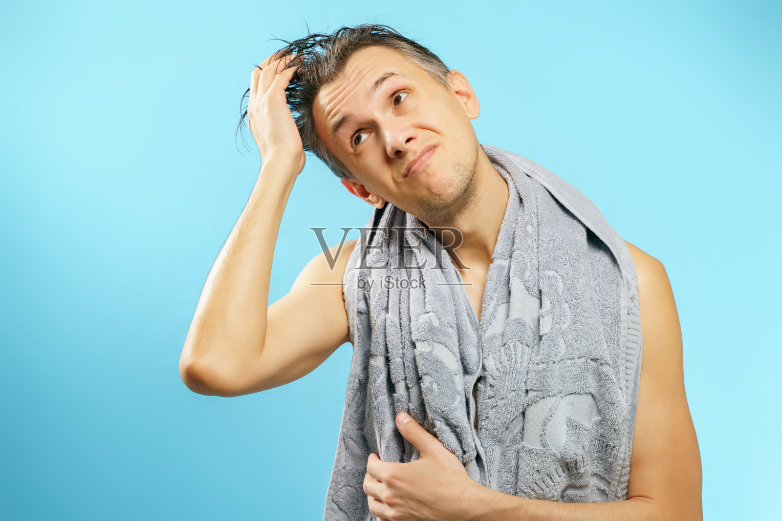 一个年轻男子的肖像与湿头发和毛巾抱着他的头在一个蓝色的背景照片摄影图片