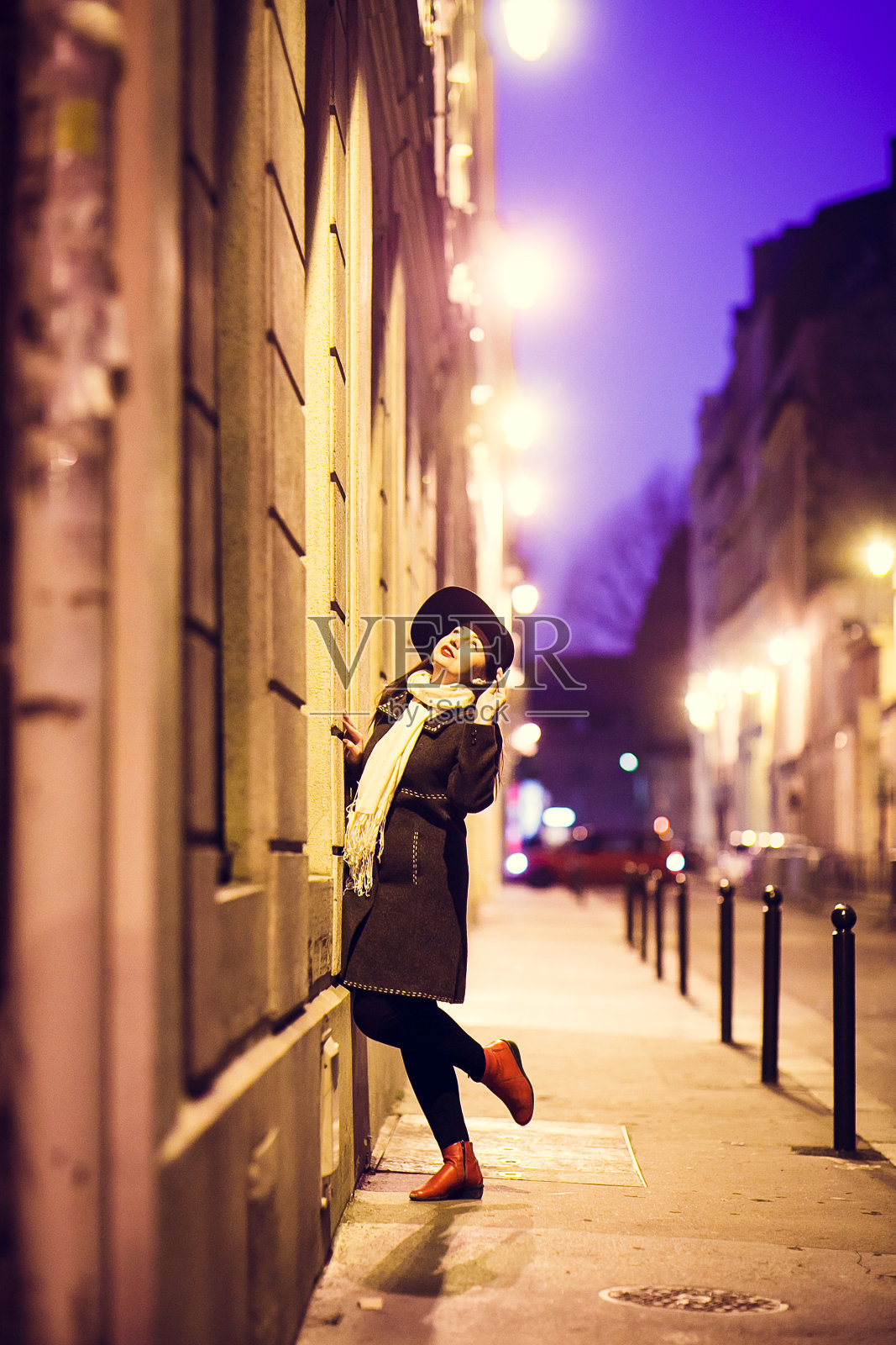戴着帽子的女孩走在巴黎夜晚的街道上。照片摄影图片