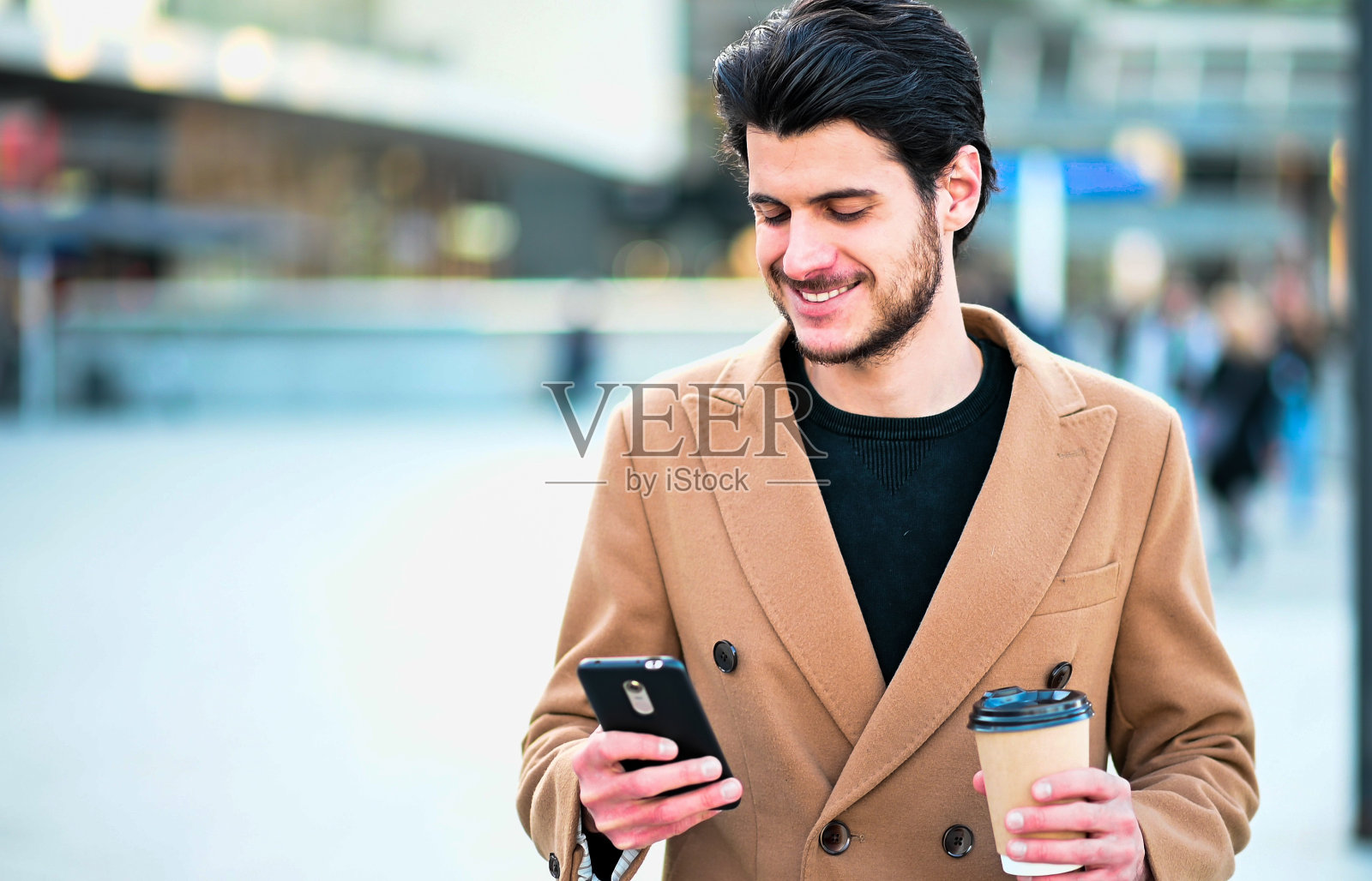 帅气优雅的男人用他的智能手机和拿着一杯咖啡照片摄影图片
