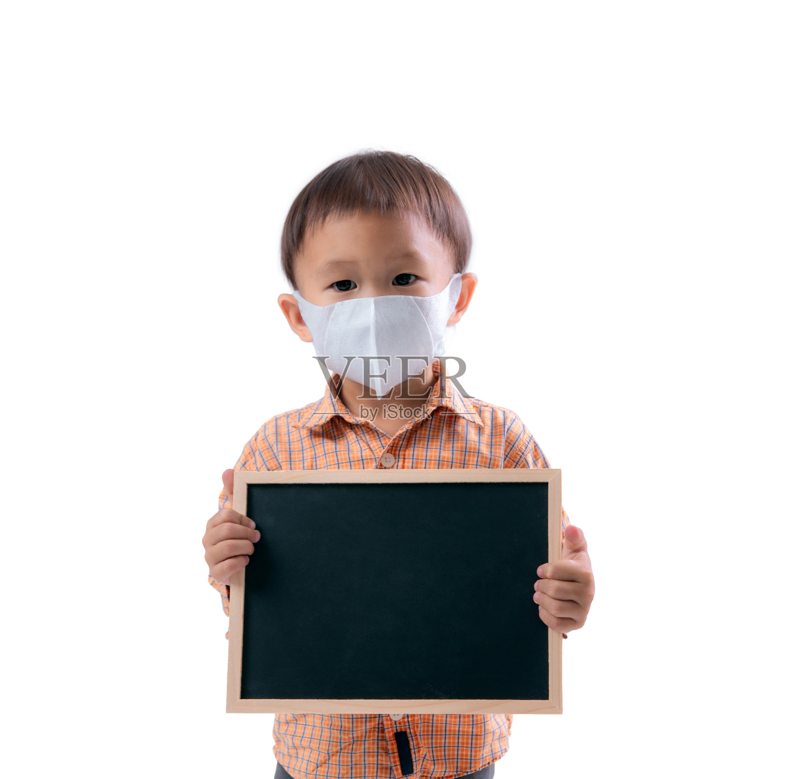 一个亚洲小孩站着，拿着一块写着空格的黑板。戴上医用口罩。照片摄影图片