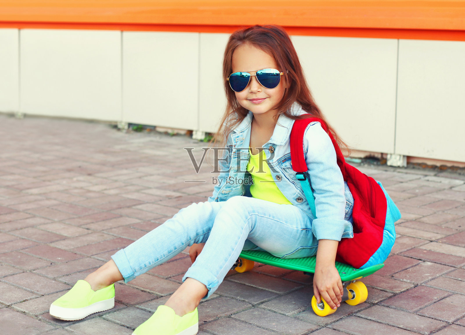 小女孩的肖像，坐在滑板与背包在城市街道上照片摄影图片