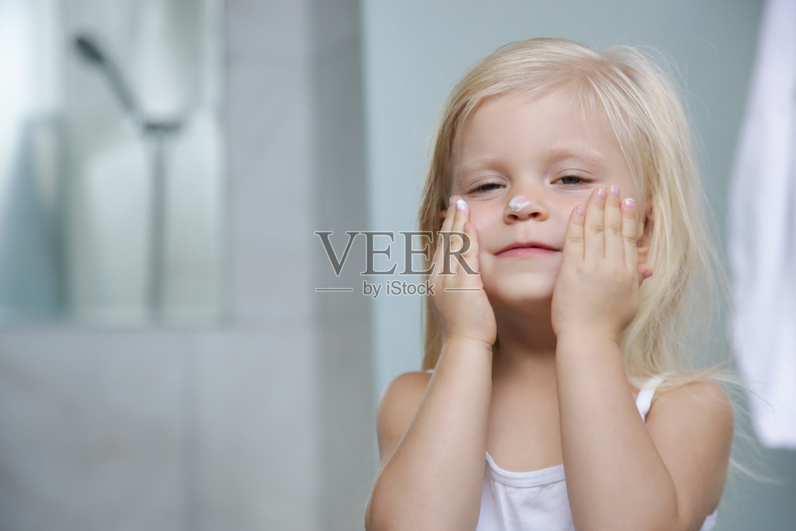 可爱的金发白种人幼童女孩在她的脸上涂抹霜照片摄影图片