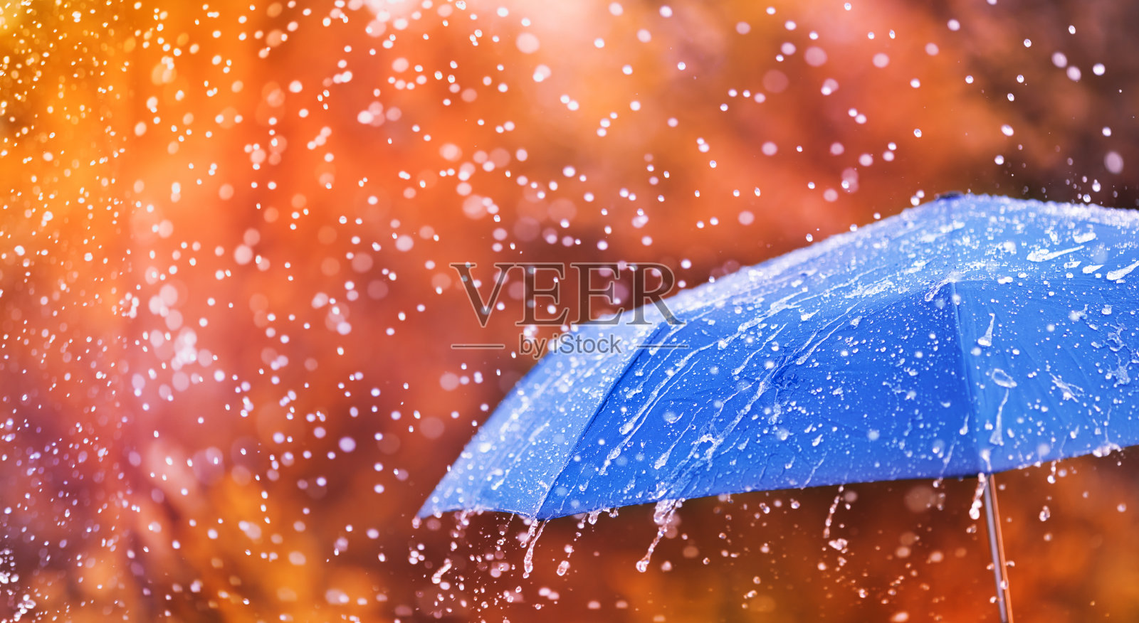 秋色带着蓝色的伞下着雨点，溅起水滴。雨天的概念。照片摄影图片