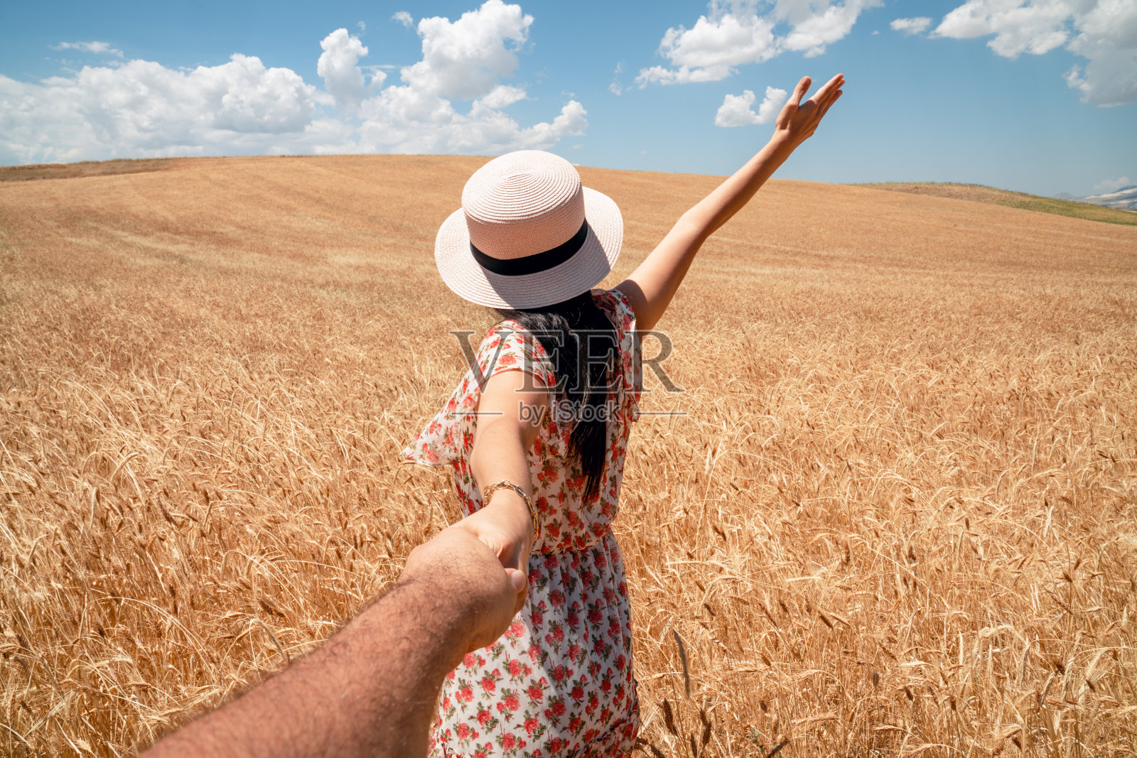 美丽的女人牵手在一个农业领域与蓝天和云彩的背景。浪漫和乡村概念。照片摄影图片