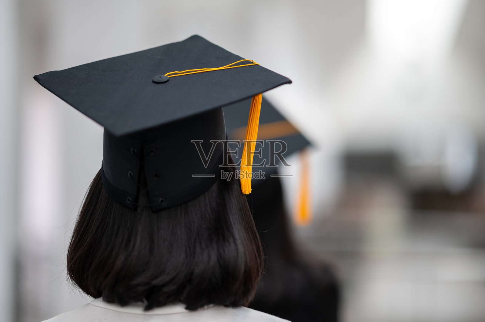戴着黑帽子，带着金黄色流苏的女毕业生正走向前面。照片摄影图片