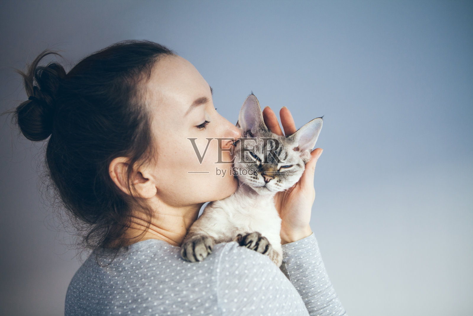 一个女人正在亲吻和拥抱她的可爱的德文雷克斯猫。照片摄影图片
