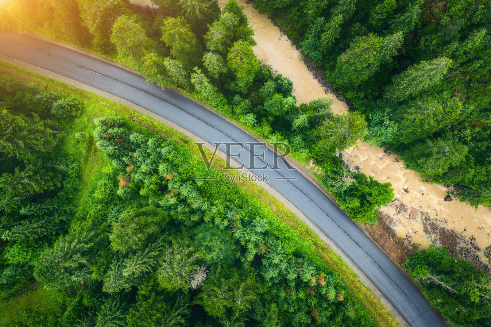 鸟瞰图的道路在美丽的绿色森林日落在夏天。喀尔巴阡山脉的道路、松树、模糊的汽车和河流构成了丰富多彩的景观。高速公路俯视图。旅行在乌克兰照片摄影图片