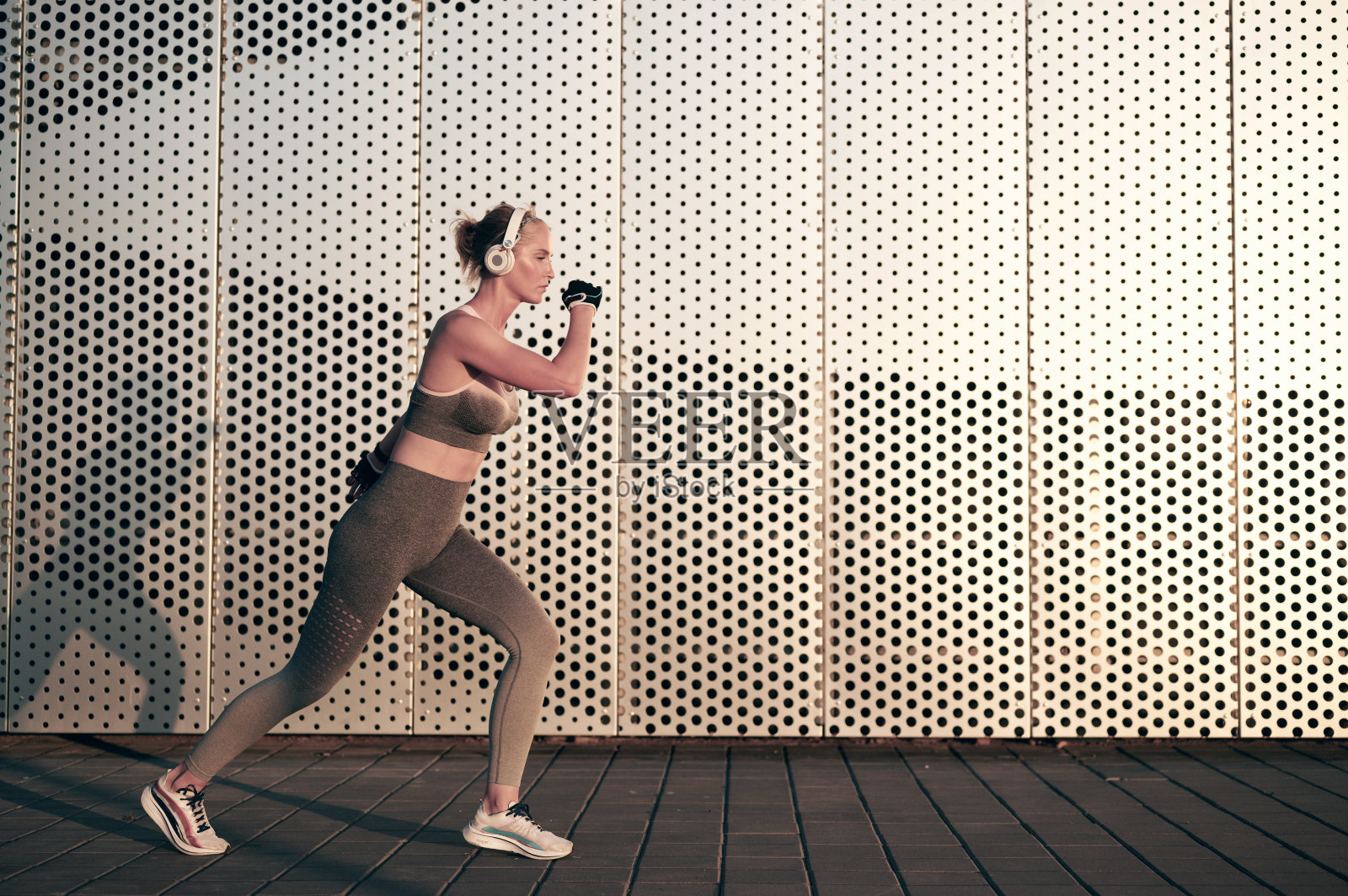 适合运动女性户外慢跑。健康的年轻女运动员在墙前做健身运动，戴着耳机听音乐照片摄影图片