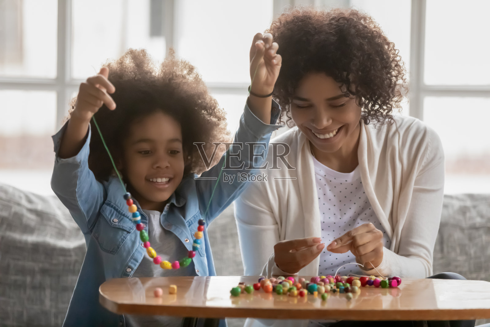 快乐的混血母亲和小女儿制作手镯照片摄影图片