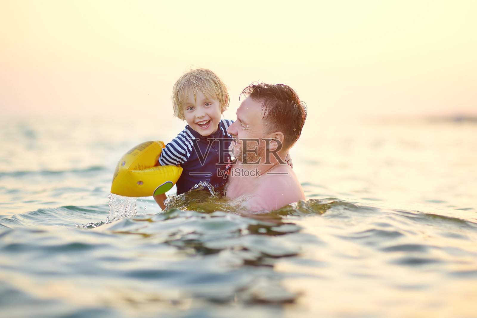 一个戴着充气臂章的学龄前男孩和他的父亲在海里游泳。有趣的海滩度假的孩子。有孩子的家庭度假。照片摄影图片