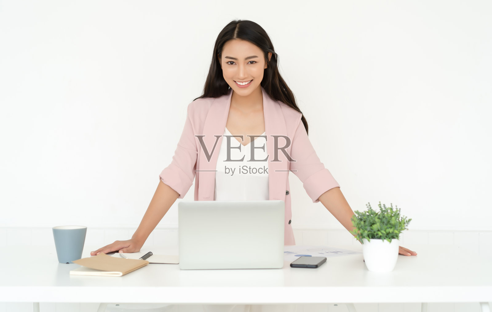 这是一个年轻漂亮的亚洲女商人在网上做小生意的照片，她站在桌子上的工作站，看着镜头。自由职业创业小企业主，在线销售。照片摄影图片