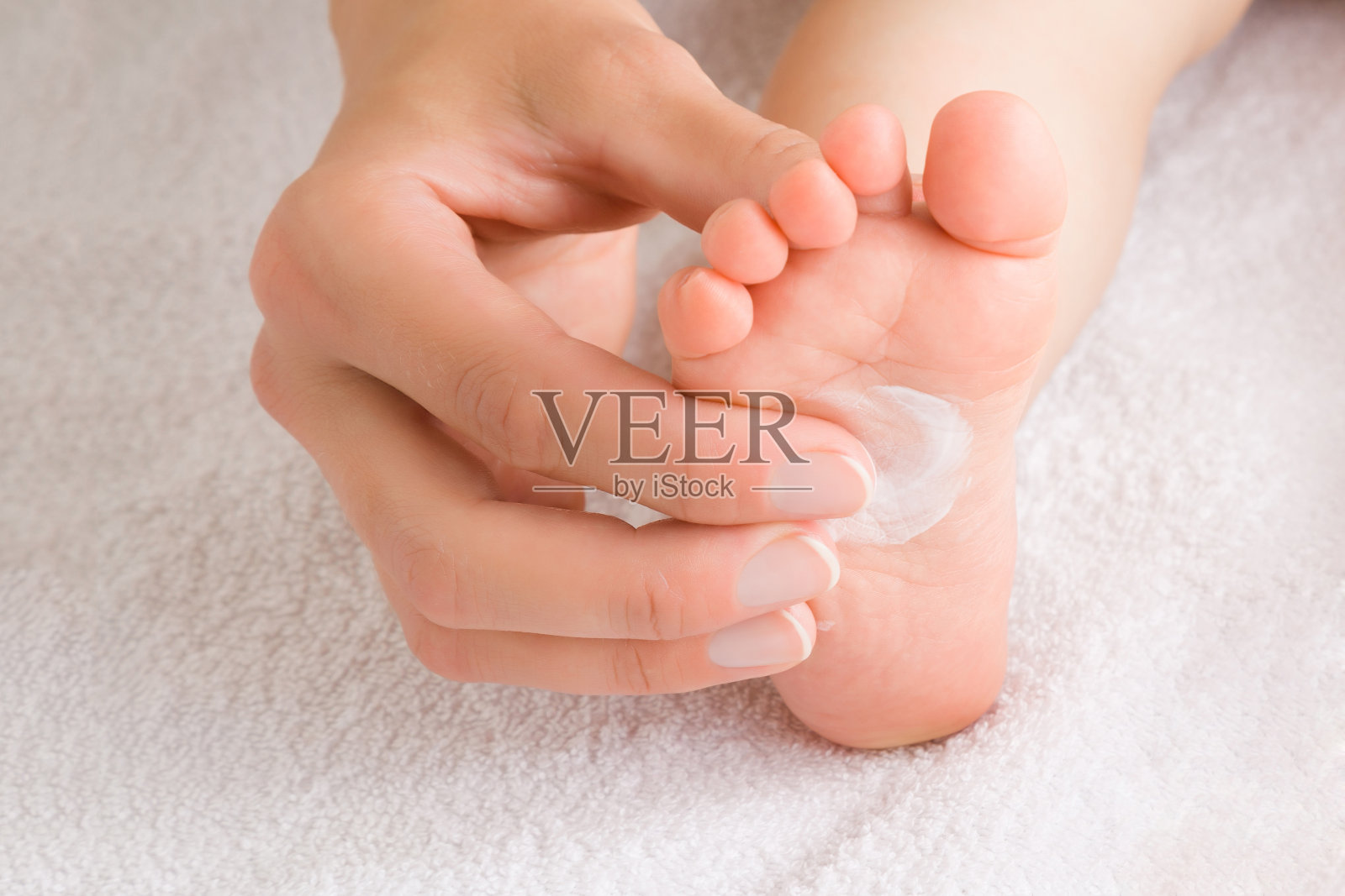 年轻的母亲用手将白色保湿霜涂在婴儿的脚上。关爱孩子洁净柔软的身体肌肤。特写镜头。前视图。照片摄影图片