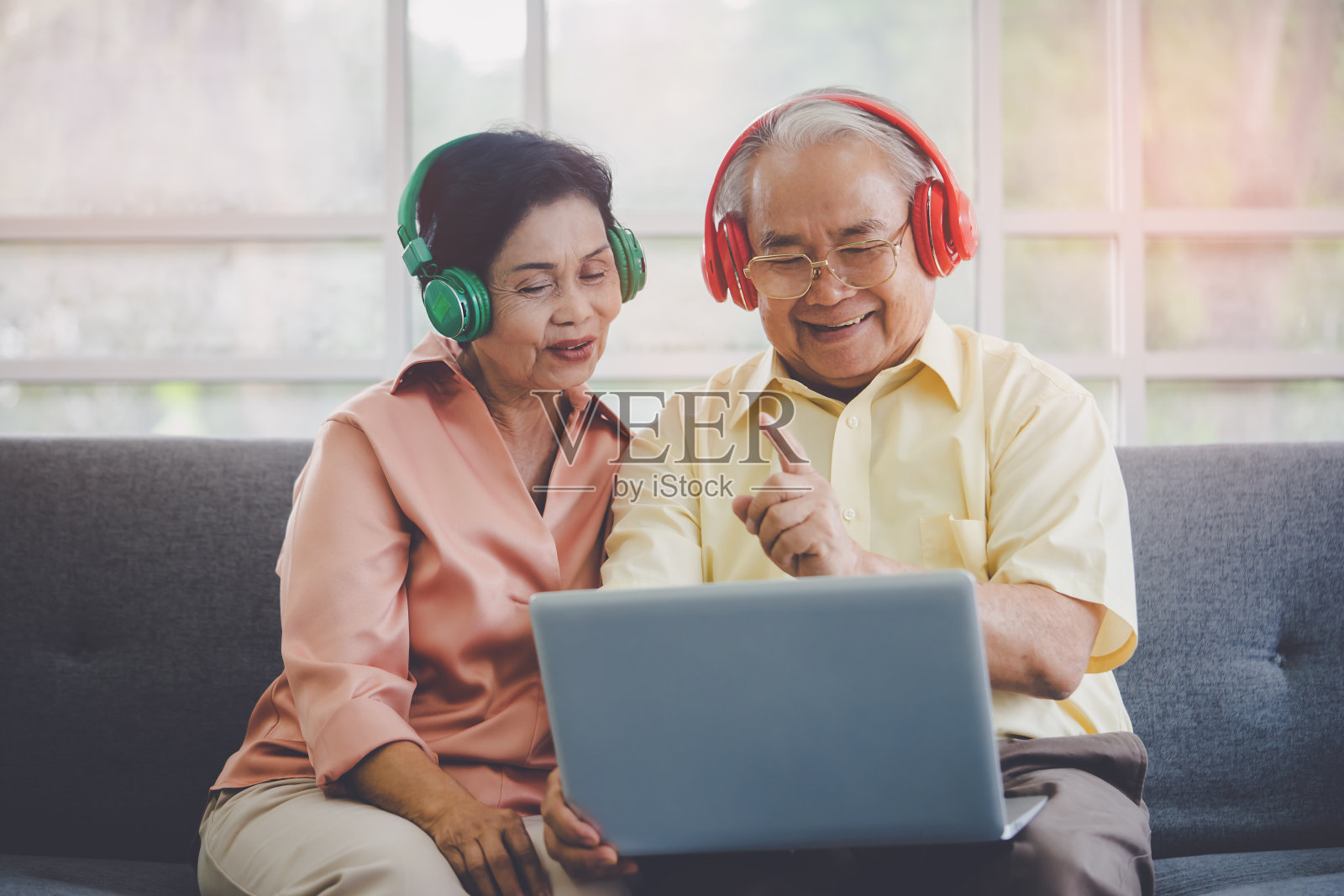 一对快乐的老夫妇正用彩色耳机在笔记本电脑上看音乐电影。照片摄影图片