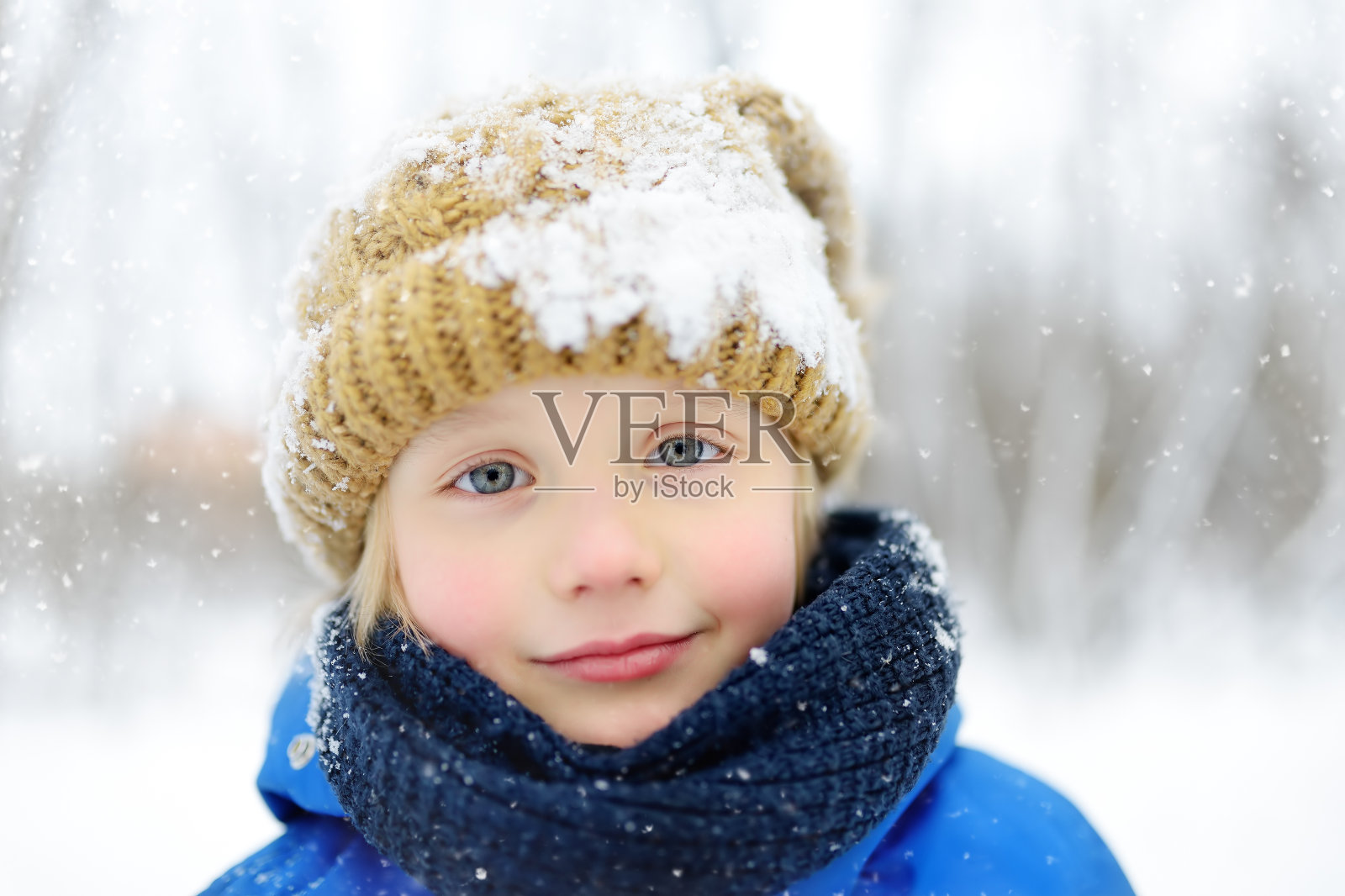 穿着蓝色冬装的有趣小男孩在下雪的时候走。儿童冬季户外活动。照片摄影图片