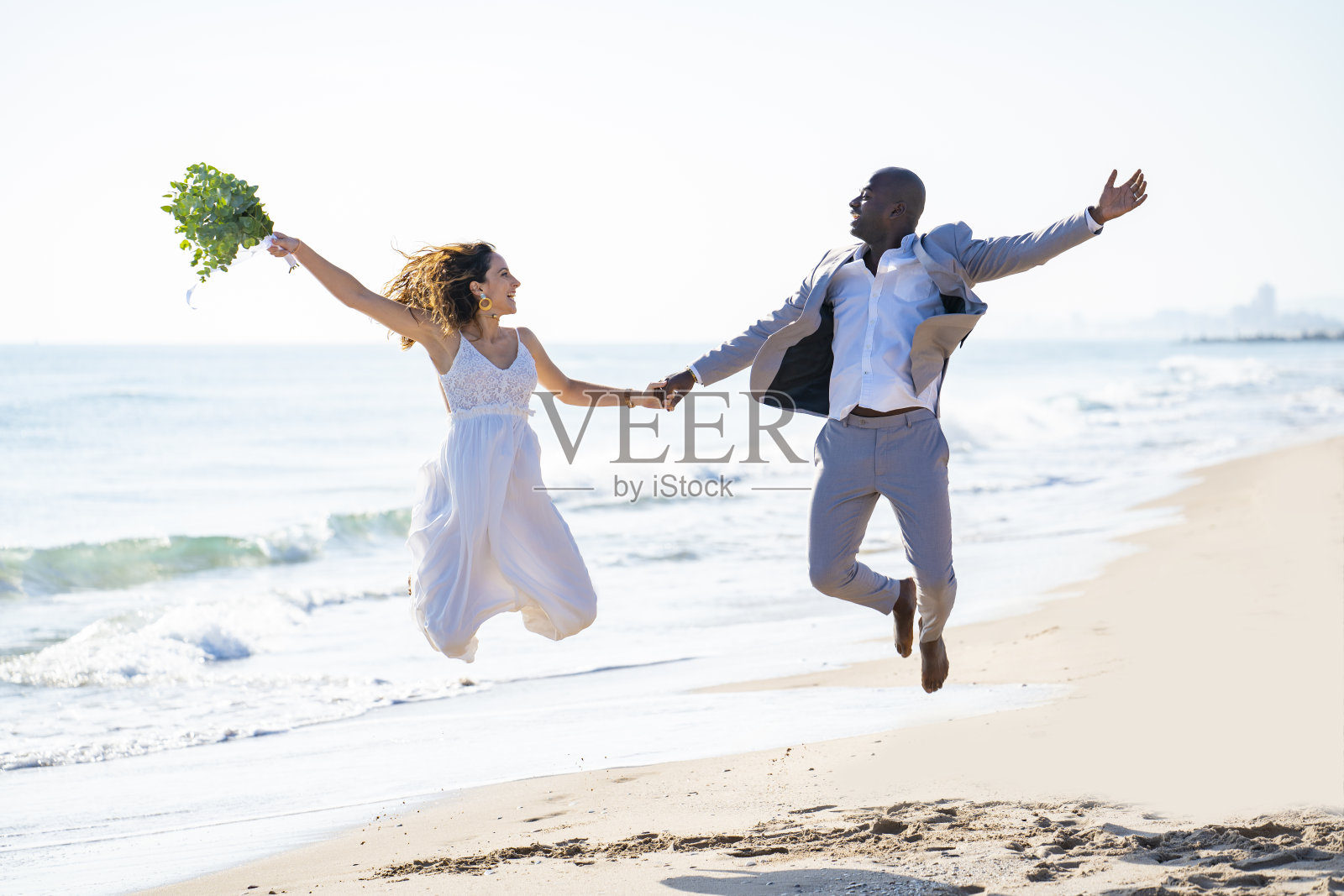 刚刚结婚度蜜月的新婚夫妇在海滩上跳高混合种族照片摄影图片