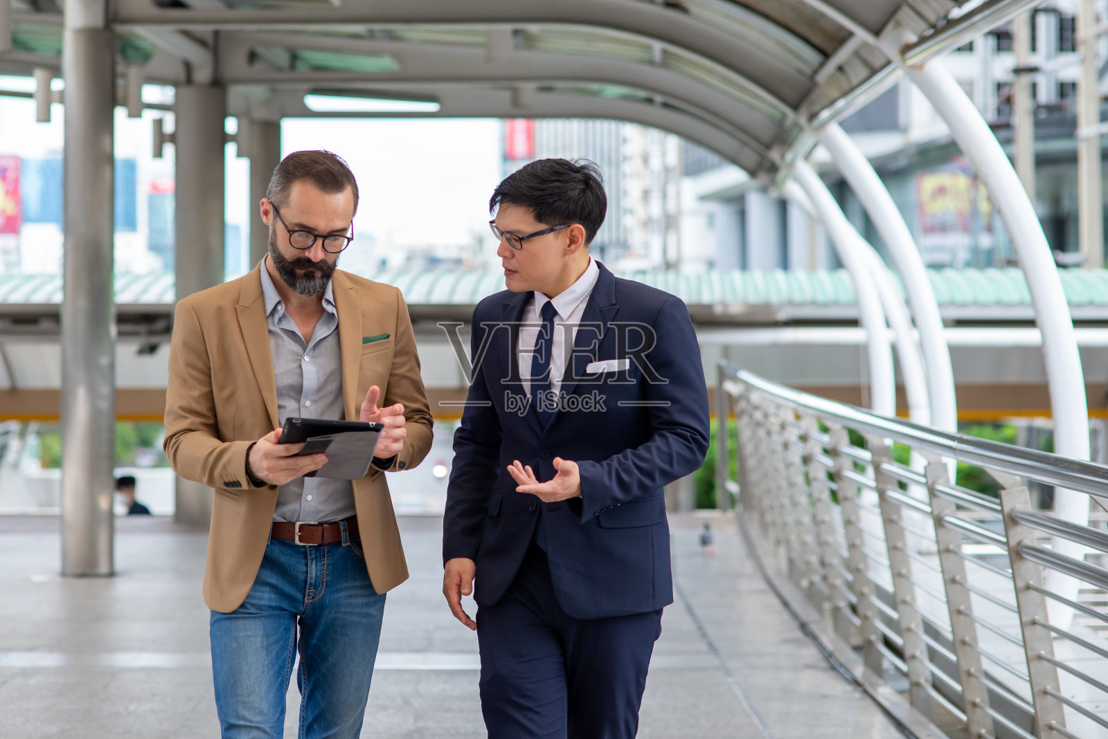 两个商务人士白种人与亚洲人同事伙伴关系讨论商业项目计划与使用数字平板电脑在城市。商务会议、技术、并购概念。照片摄影图片