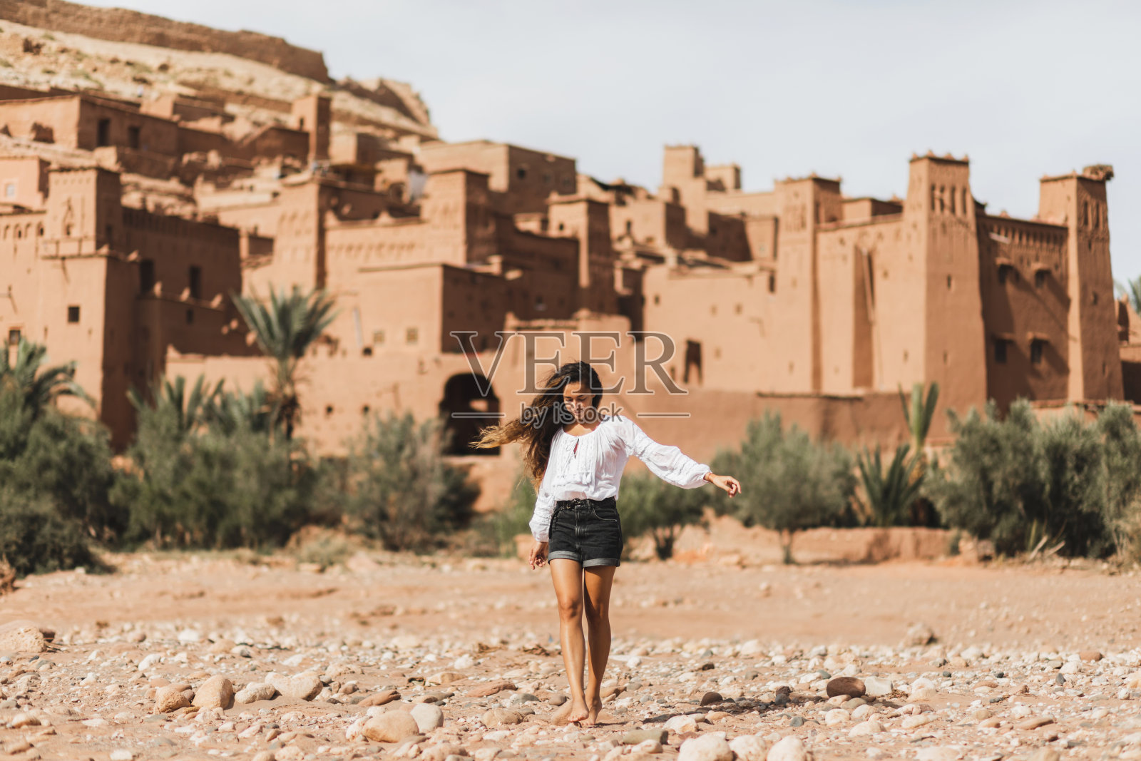 年轻的卷发女人东方人的外表走在卡斯巴艾特本哈杜的背景。去摩洛哥旅行，瓦尔扎扎特。暑期度假，旅游生活理念。照片摄影图片