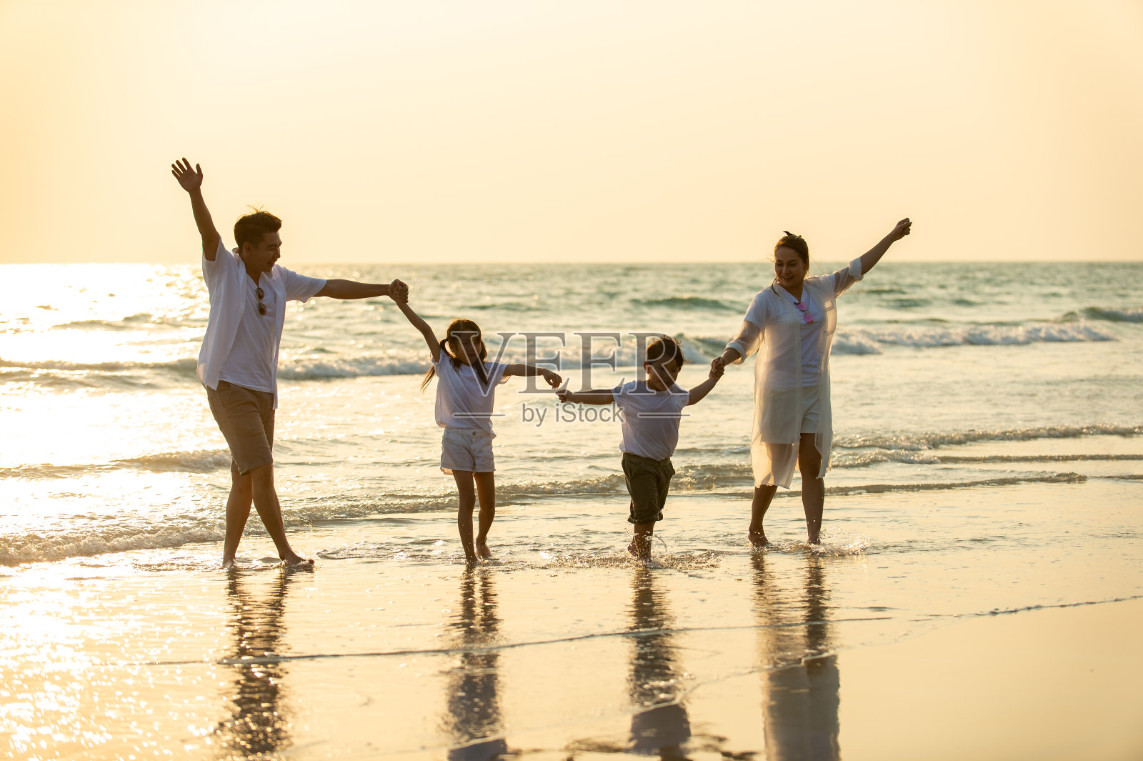 幸福的亚洲家庭父母和两个孩子的男孩和女孩手牵手一起走在海滩上在夏天的日落。父亲，母亲和孩子享受和有乐趣的户外假期假期。照片摄影图片
