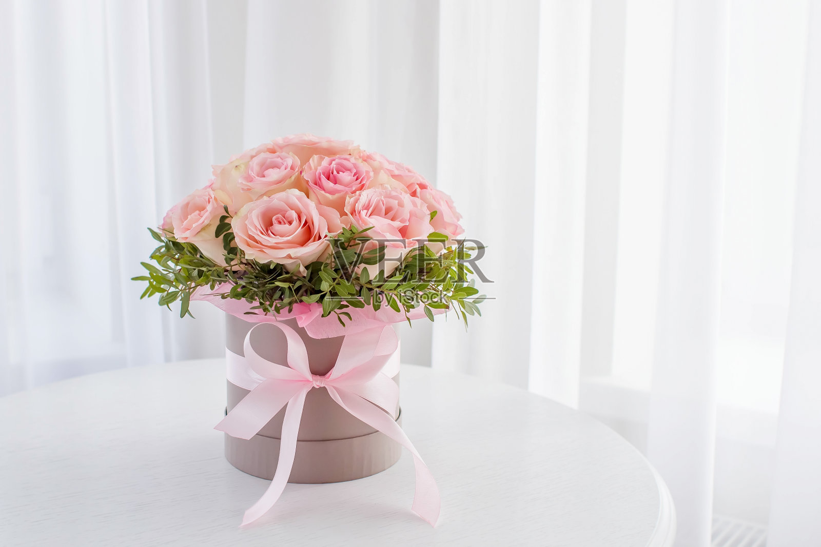 白色的桌子上，一束美丽的粉红色玫瑰，装在一个喜庆的圆盒子里。节日礼物，生日，婚礼，母亲节，情人节，妇女节。帽子盒里的花。照片摄影图片