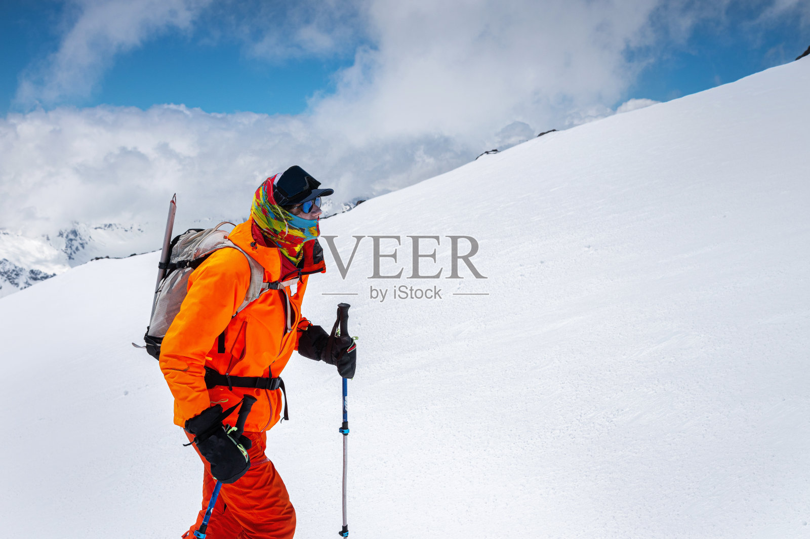 一个严峻的登山滑雪者的肖像戴着太阳镜和一顶戴着滑雪面罩的帽子在他的脸上。以厄尔布鲁斯山为背景照片摄影图片
