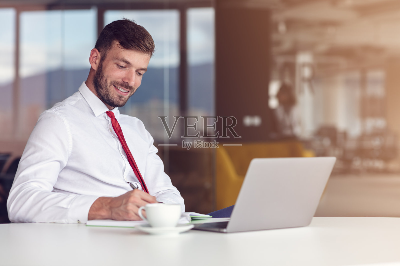办公室便装日。微笑的男性员工使用笔记本电脑和喝咖啡。照片摄影图片