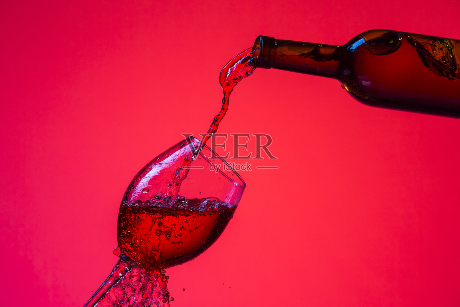 葡萄酒倒出的瓶子在右手边的嘶鸣杯与彩色液体，滴和滴。水平图像组成照片摄影图片