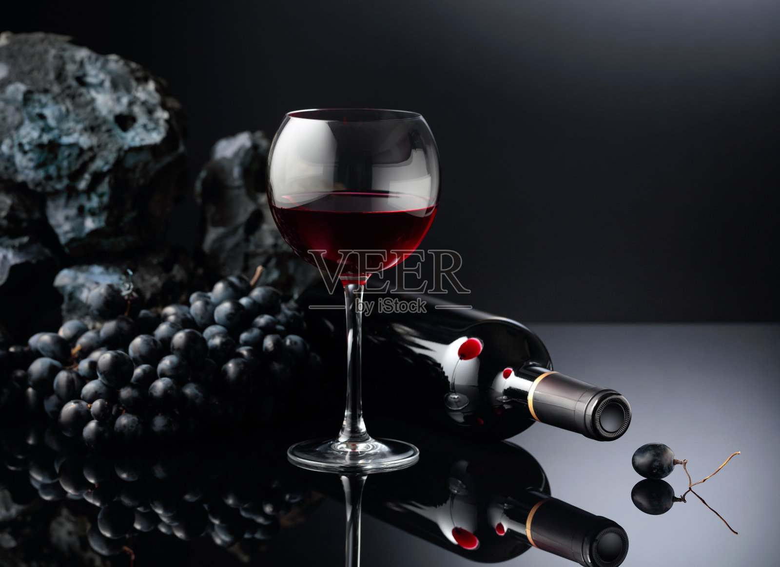 蓝色的葡萄和红酒在黑色的反光背景上。照片摄影图片